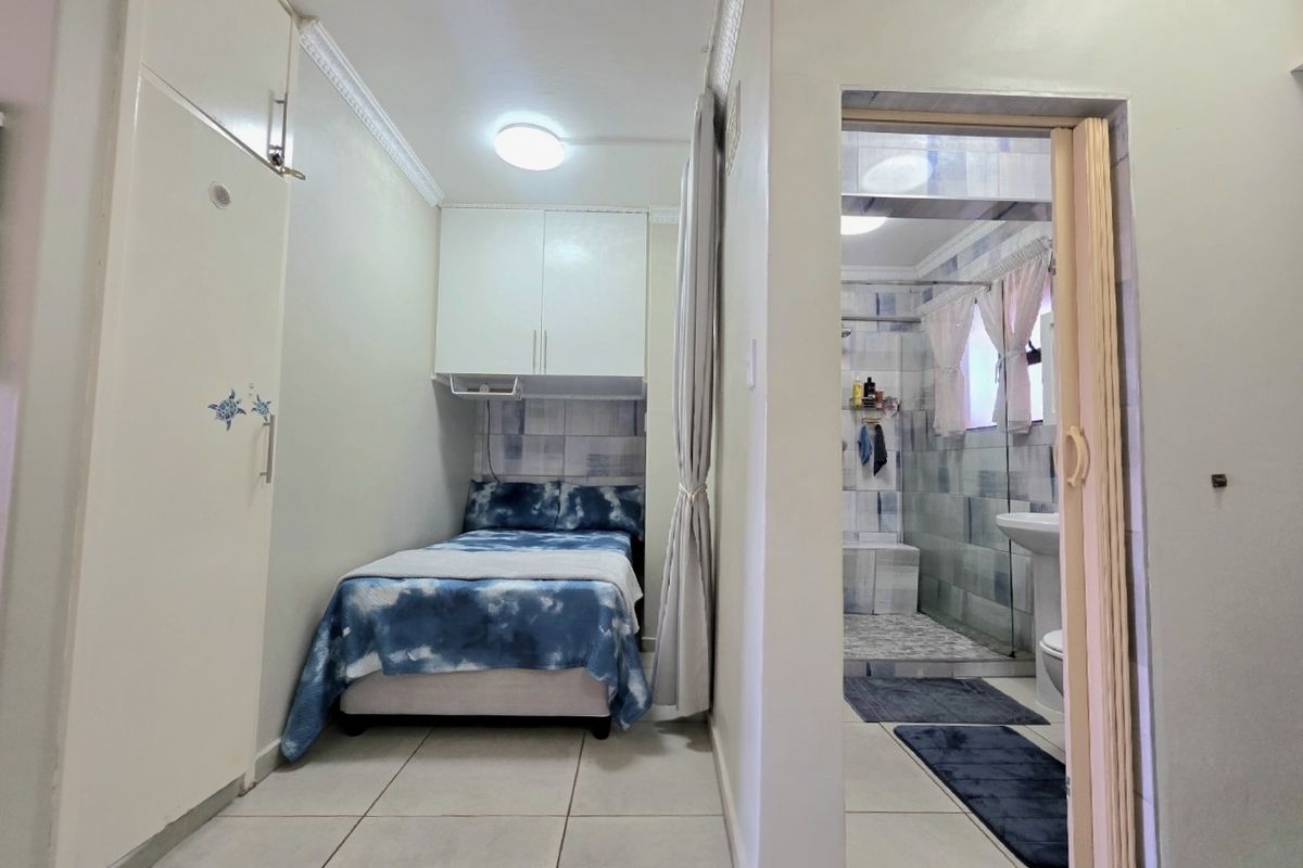 A compact bedroom featuring built-in cupboards, tiled flooring, and direct access to an en-suite bathroom with a shower.