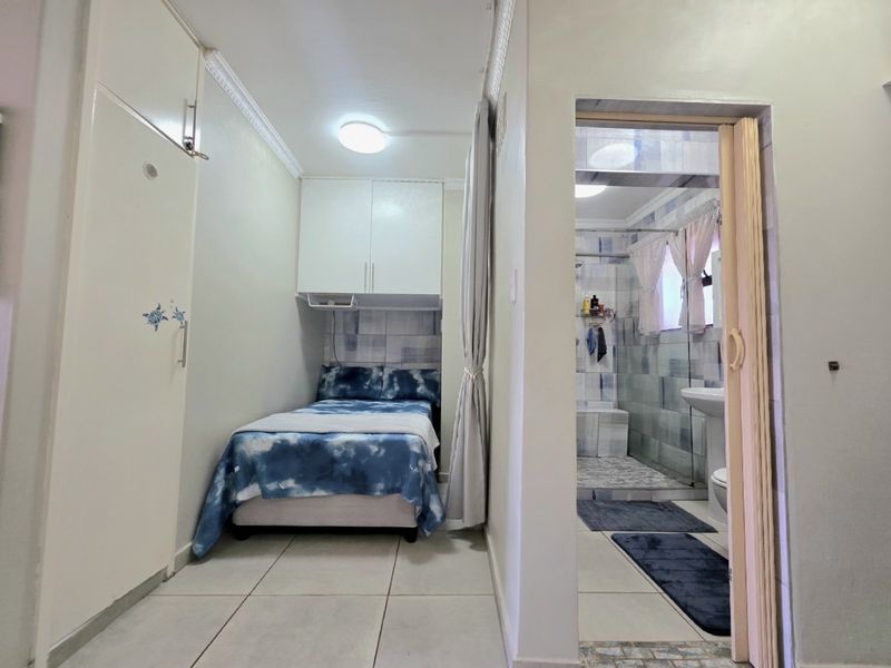 A compact bedroom featuring built-in cupboards, tiled flooring, and direct access to an en-suite bathroom with a shower.