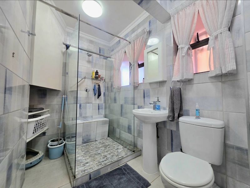 A functional bathroom featuring a pedestal basin, a glass-enclosed shower with a built-in bench, and tiled finishes throughout.