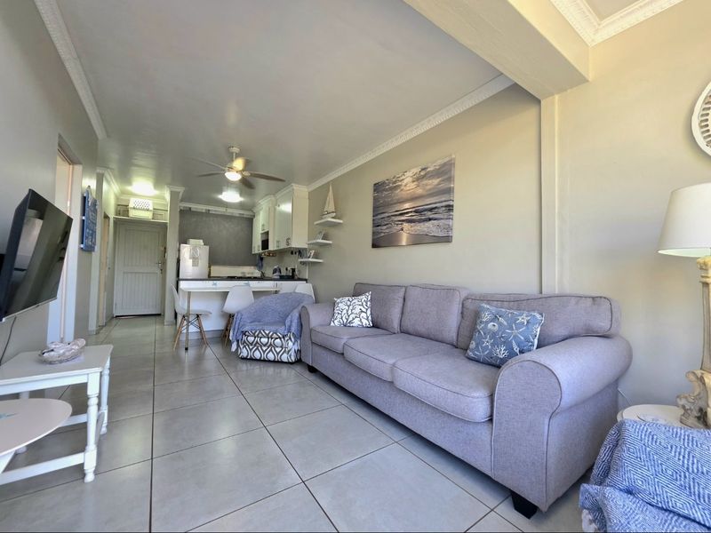 Open-plan living area featuring tiled flooring, crown molding, and a compact kitchen with a breakfast counter and ceiling fan.