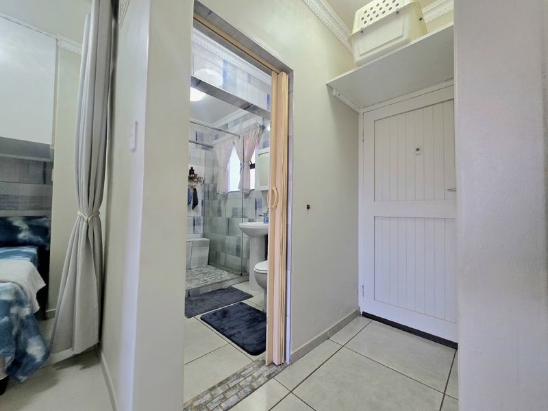 A hallway area featuring tiled flooring and built-in shelving, providing access to an adjacent bathroom with a pedestal basin and shower enclosure.