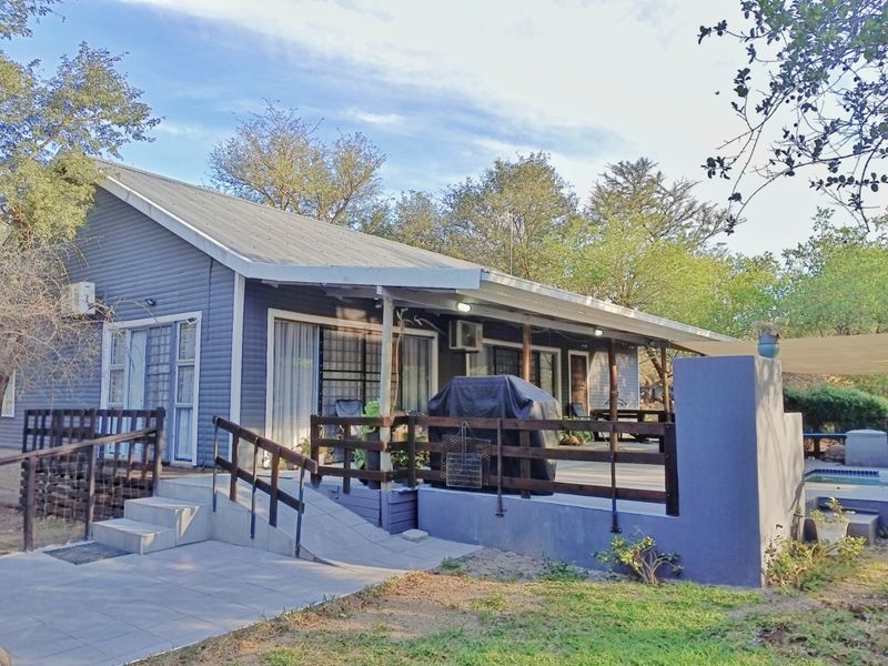 Rear view of the property featuring a covered timber deck, wheelchair access ramp, and an adjacent swimming pool area set in a natural garden.