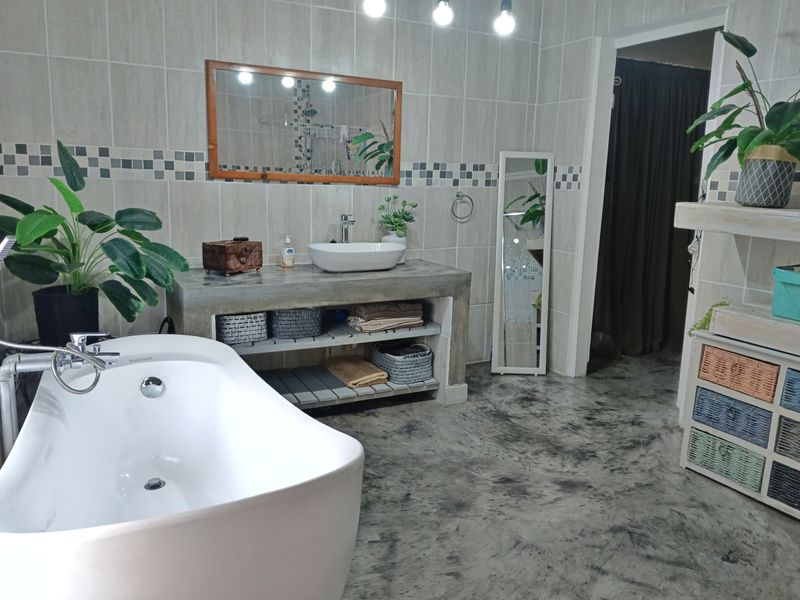 Modern bathroom featuring a freestanding bathtub, custom concrete vanity with vessel sink, and polished concrete flooring with neutral wall tiling.