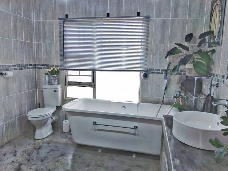 A well-appointed bathroom featuring a freestanding bathtub, modern vessel sink, and neutral wall tiling with a decorative border.