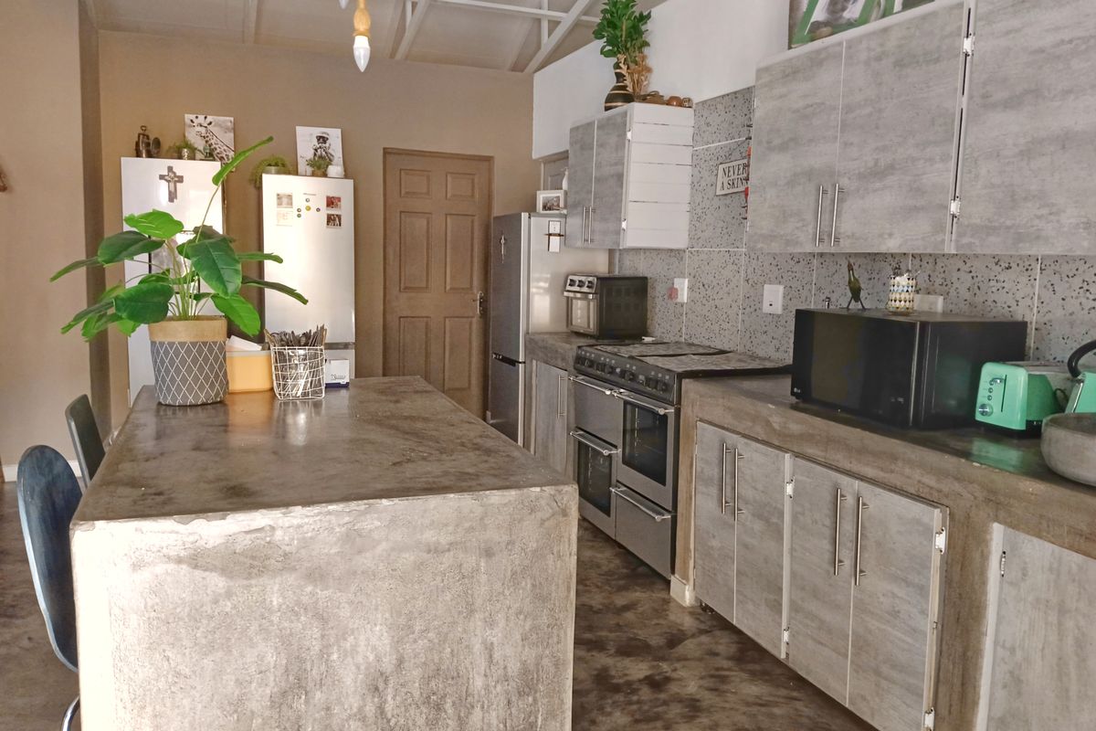 A rustic-style kitchen featuring concrete countertops, a central concrete island, laminated cabinetry, and exposed roof trusses.