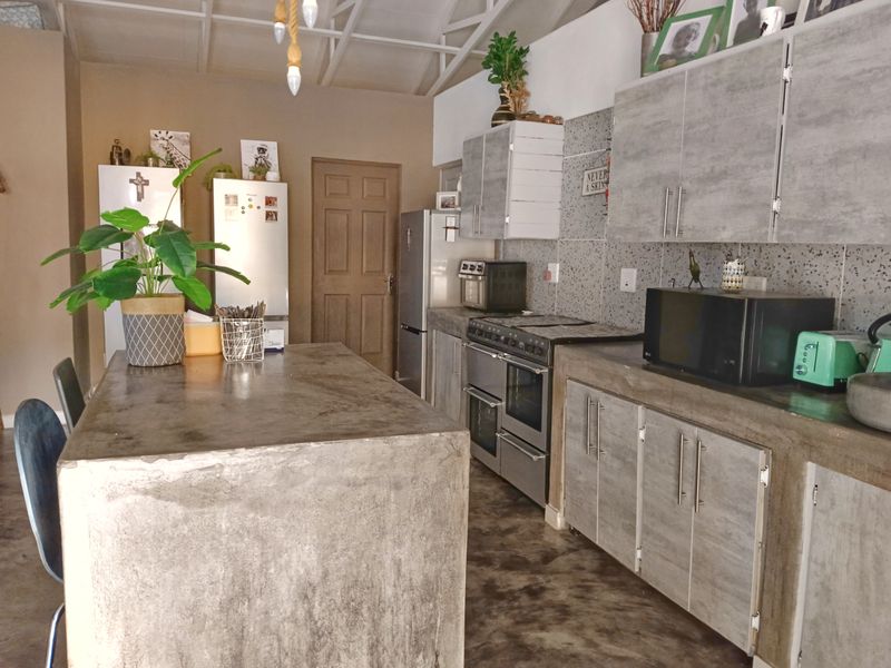 A rustic-style kitchen featuring concrete countertops, a central concrete island, laminated cabinetry, and exposed roof trusses.