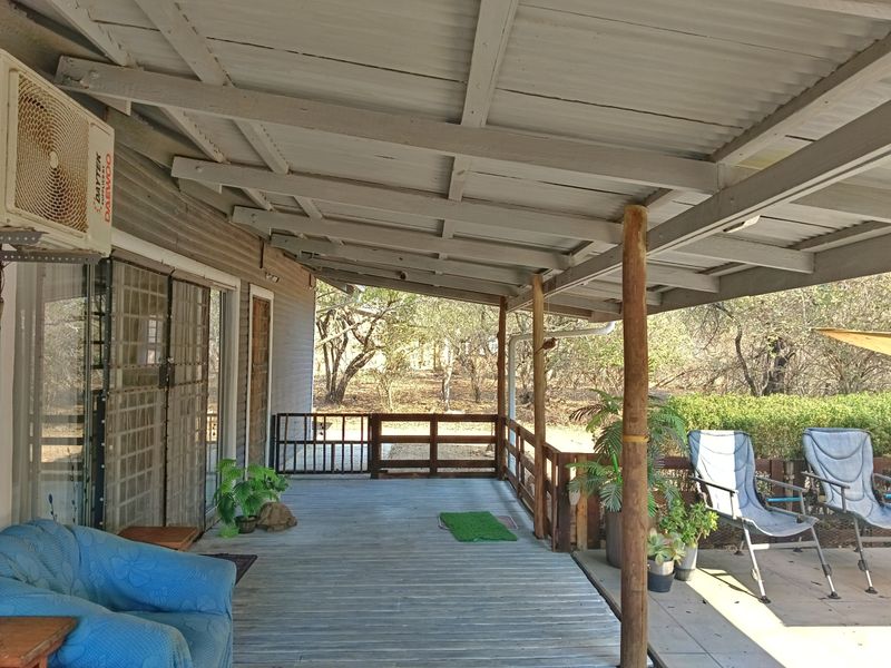 A covered outdoor timber deck featuring a corrugated roof, timber balustrades, and direct access to the home via sliding glass doors.