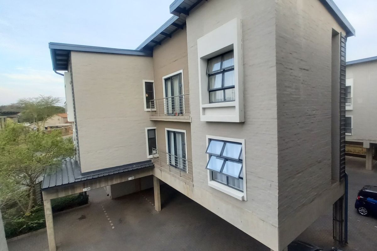 Exterior view of a modern apartment building featuring painted brick walls, metal balcony railings, and integrated covered parking bays.