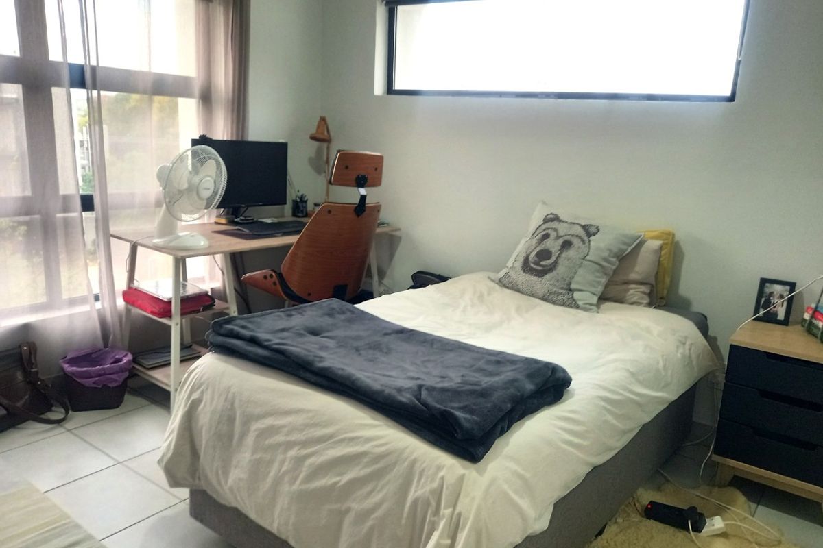A functional bedroom featuring tiled flooring, a large window for natural light, and an additional clerestory window.