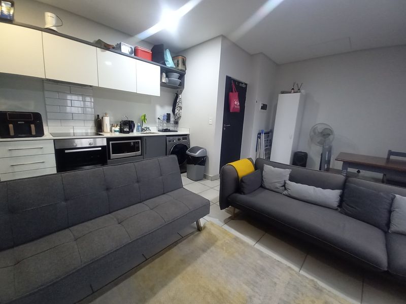 Open-plan living area featuring a compact kitchen with built-in cabinetry, electric oven, hob, and tiled flooring throughout.