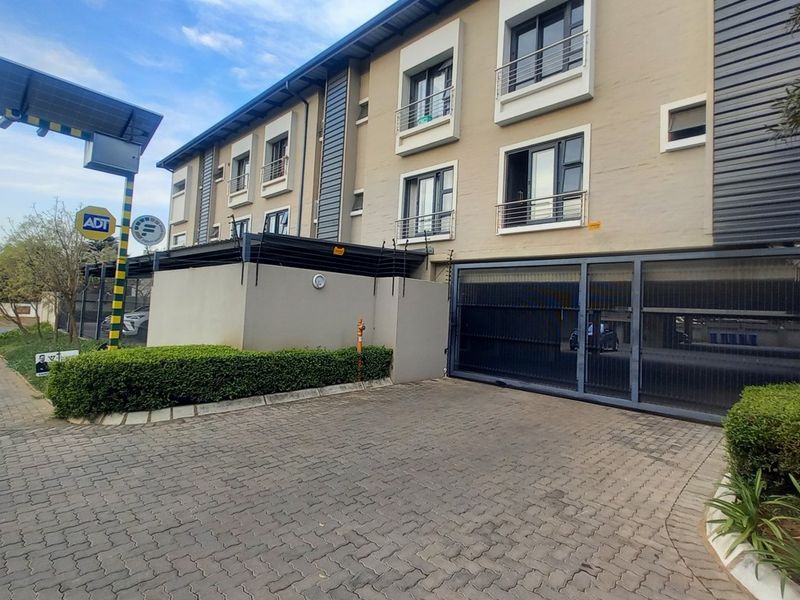 Front exterior view of the apartment complex featuring a paved driveway, secure automated gate access, electric fencing, and well-maintained landscaping.