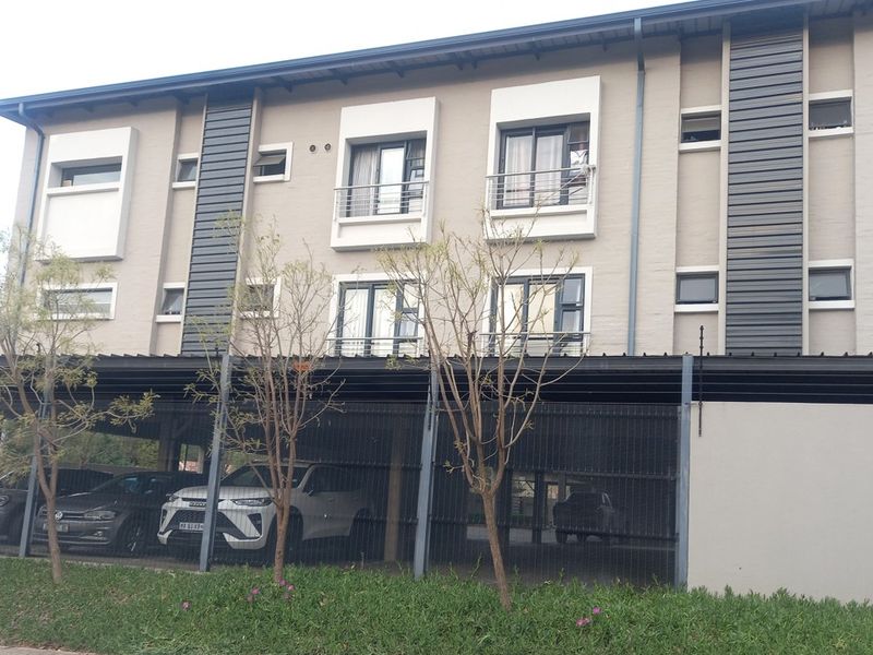 Front elevation of a multi-story apartment building featuring covered parking bays, modern facade finishes, and balconies with metal railings.