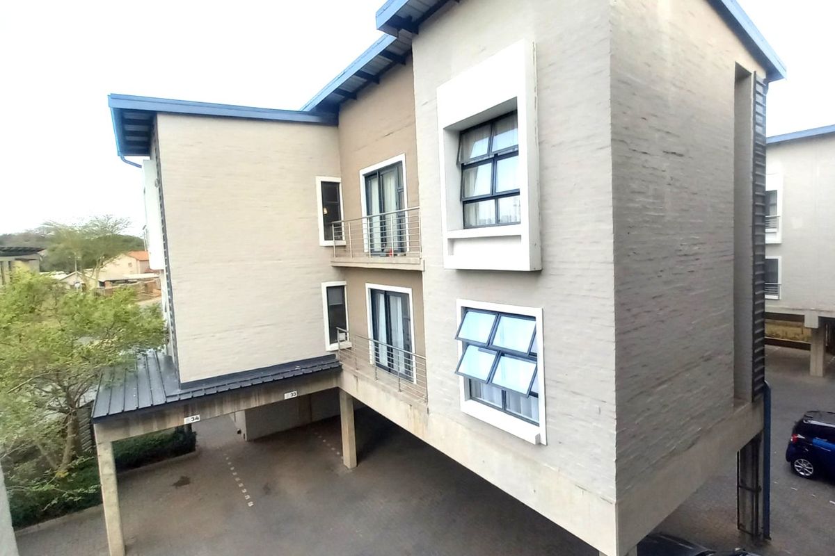 Exterior view of a multi-story apartment building featuring painted brick walls, metal balcony railings, and covered ground-level parking.