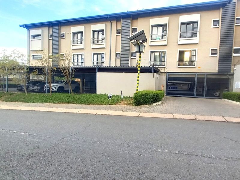 Front elevation of a multi-story apartment complex featuring covered parking, secure gated access, and balconies on upper levels.