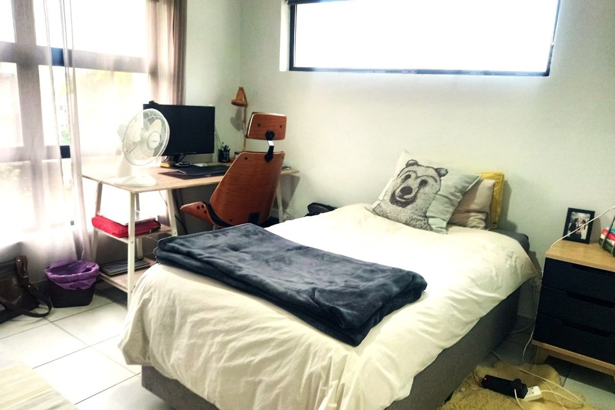 A functional bedroom featuring tiled flooring, a horizontal clerestory window, and a large sliding glass door providing natural light.