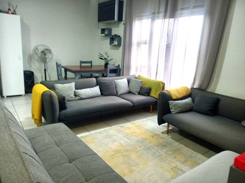 A living room area featuring tiled flooring, a wall-mounted air conditioning unit, and large windows allowing natural light.