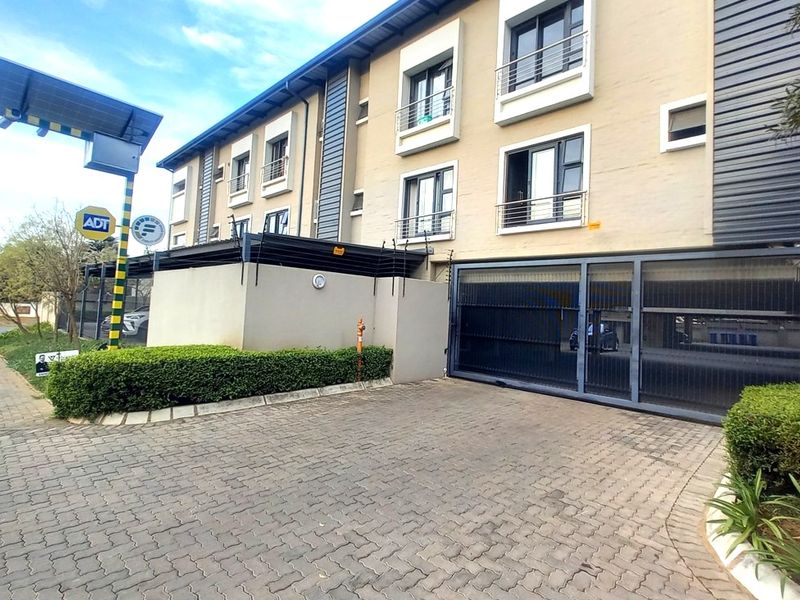 Front exterior view of the apartment complex featuring a paved driveway, secure electric gate access, perimeter walling with electric fencing, and modern balcony structures.