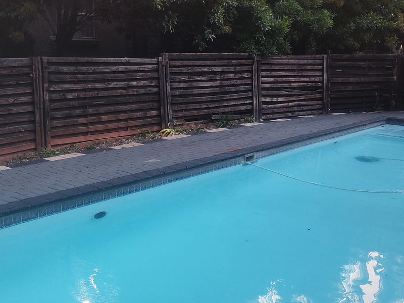Outdoor pool area featuring a paved surround and timber slat boundary fencing.