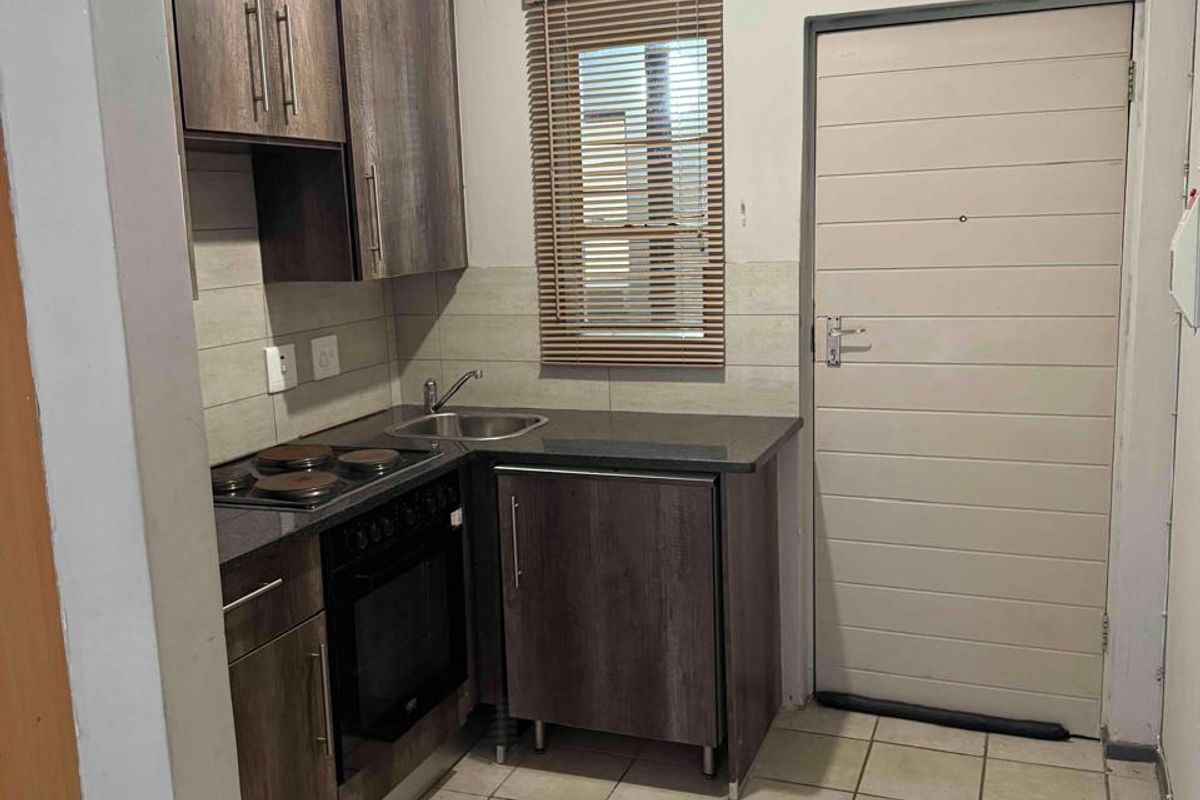 Compact kitchen featuring dark wood-look cabinetry, built-in oven and hob, stainless steel sink, and tiled flooring with a neutral backsplash.