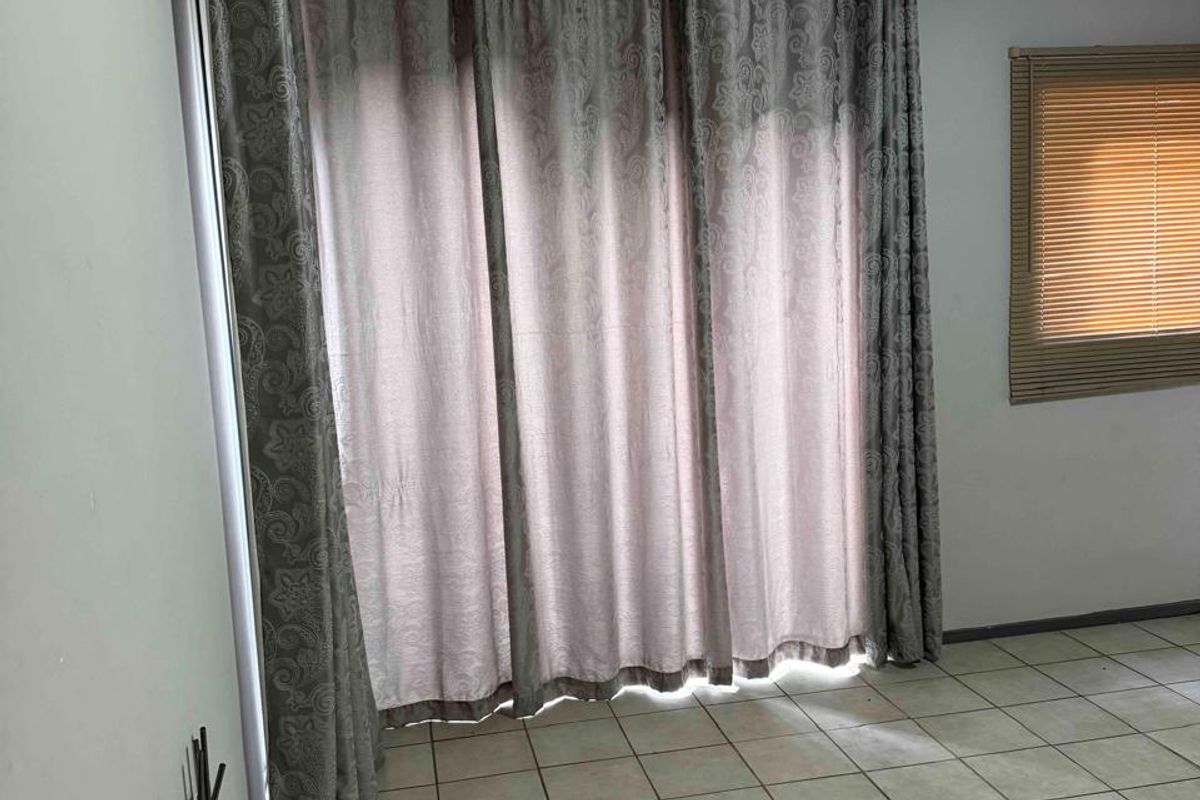 An empty living area featuring tiled flooring, large window treatments, and venetian blinds, offering a blank canvas for potential interior updates.