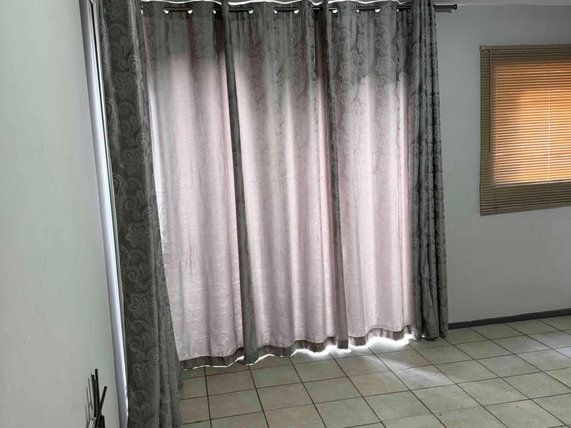 An empty living area featuring tiled flooring, large window treatments, and venetian blinds, offering a blank canvas for potential interior updates.