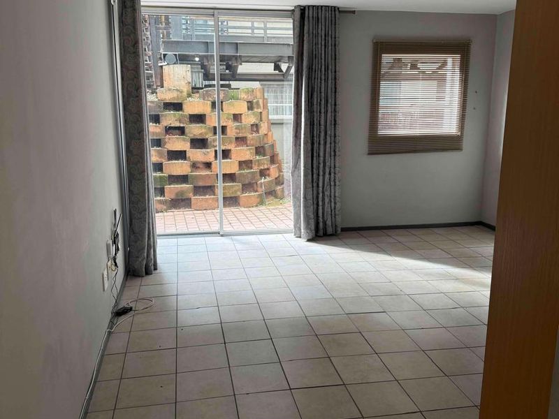 An empty living room featuring tiled flooring, a sliding glass door leading to an outdoor area, and a window with fitted blinds.