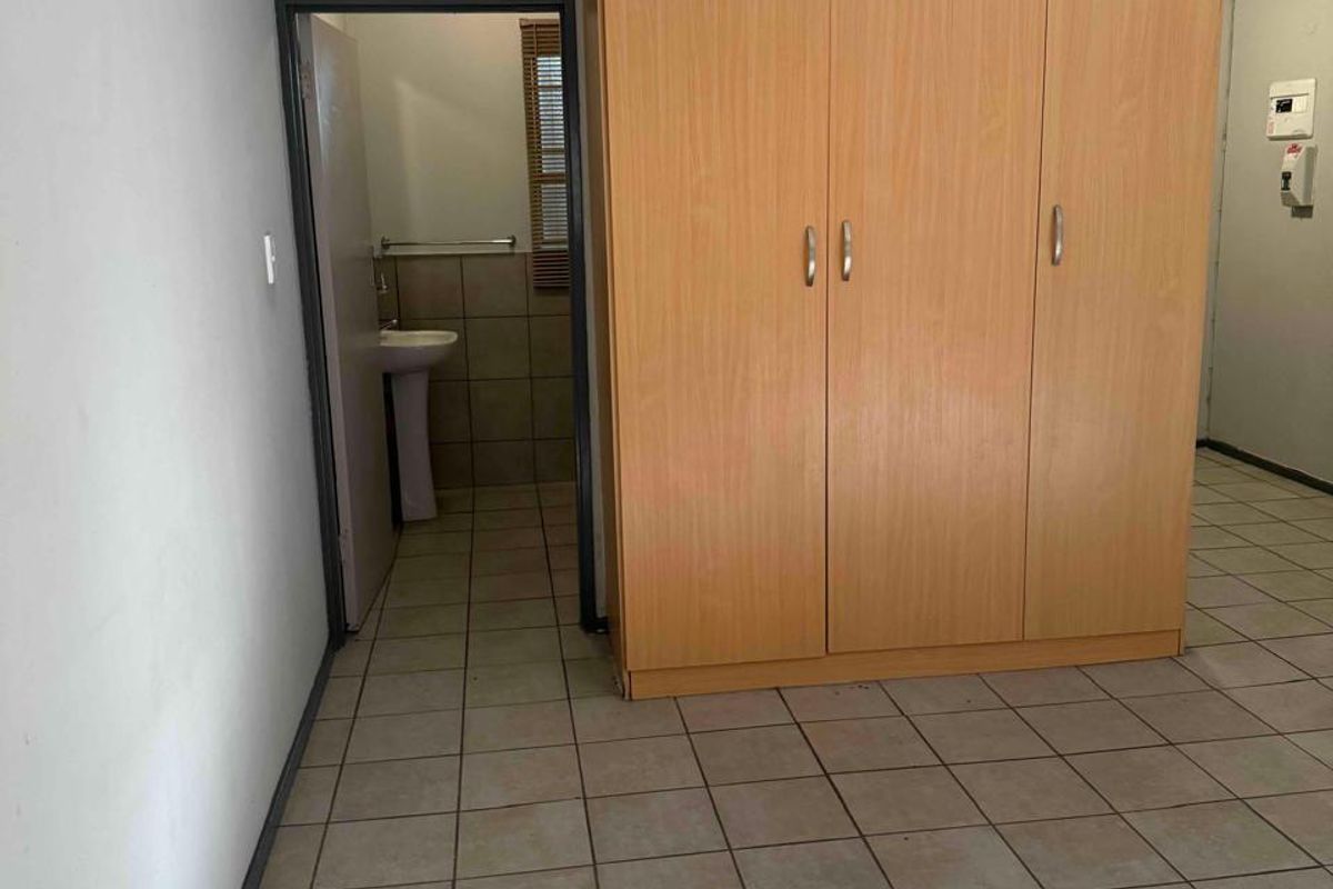 A bedroom featuring tiled flooring and a built-in wardrobe, with an adjoining en-suite bathroom area containing a pedestal basin.