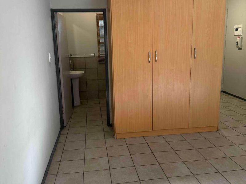 A bedroom featuring tiled flooring and a built-in wardrobe, with an adjoining en-suite bathroom area containing a pedestal basin.