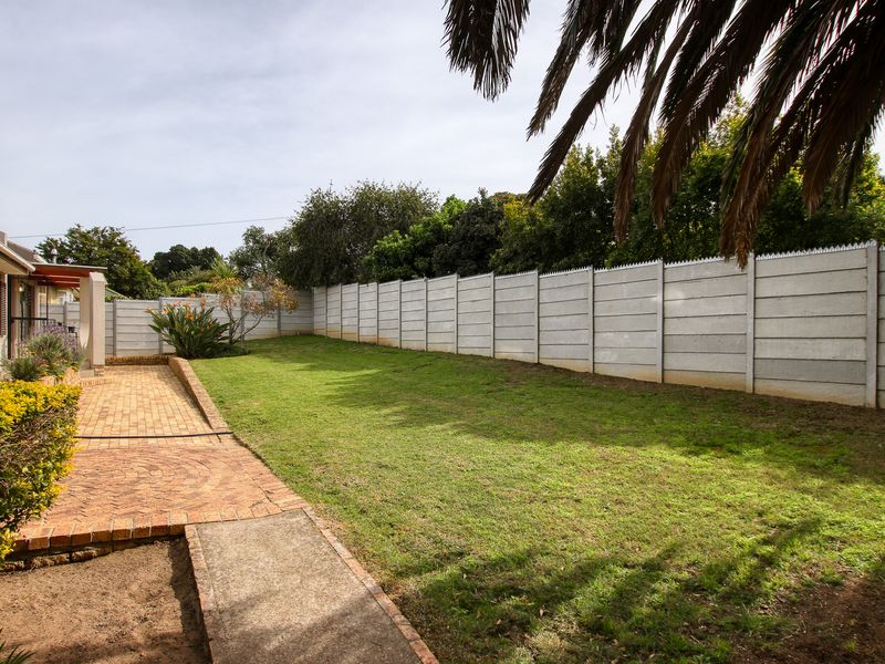 A spacious rear garden featuring a brick-paved patio, a well-maintained lawn, and secure precast concrete boundary walls.