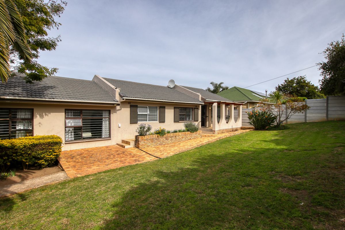 Rear view of the house featuring a paved patio area, brick planter box, and a well-maintained lawn with concrete boundary walling.