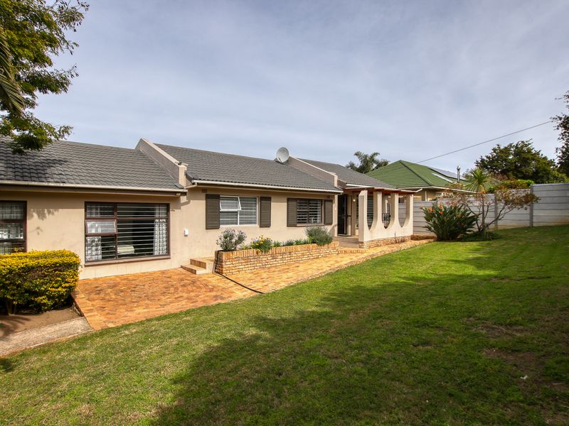 Rear view of the house featuring a paved patio area, brick planter box, and a well-maintained lawn with concrete boundary walling.