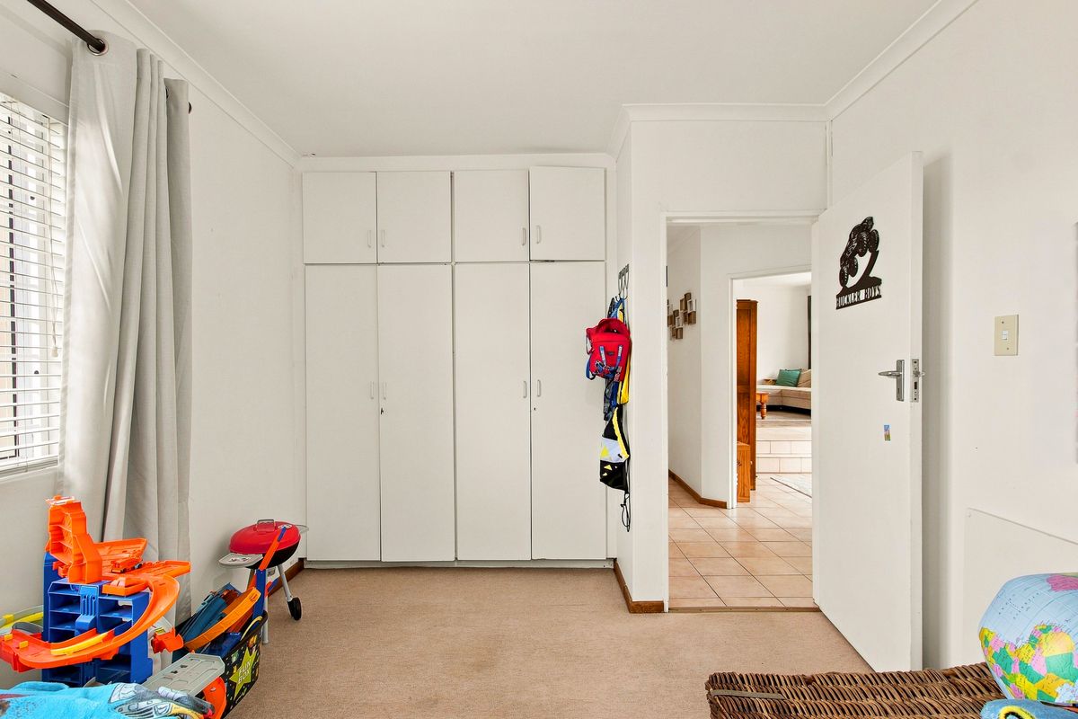 A bedroom featuring neutral carpet flooring, white walls, and a large built-in wardrobe with overhead storage cupboards.