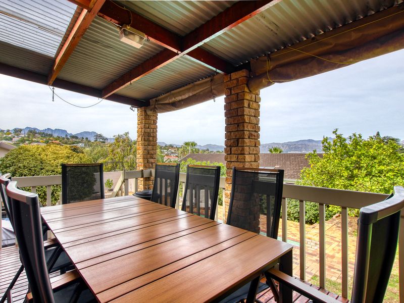 Covered outdoor patio featuring timber decking, brick columns, and a corrugated metal roof, offering elevated views of the surrounding neighborhood and mountains.