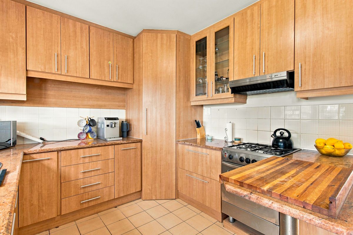 Functional kitchen featuring wood-look laminate cabinetry, granite countertops, a gas hob with extractor fan, and tiled flooring.