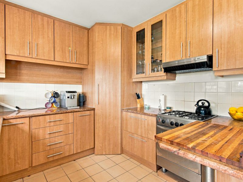 Functional kitchen featuring wood-look laminate cabinetry, granite countertops, a gas hob with extractor fan, and tiled flooring.