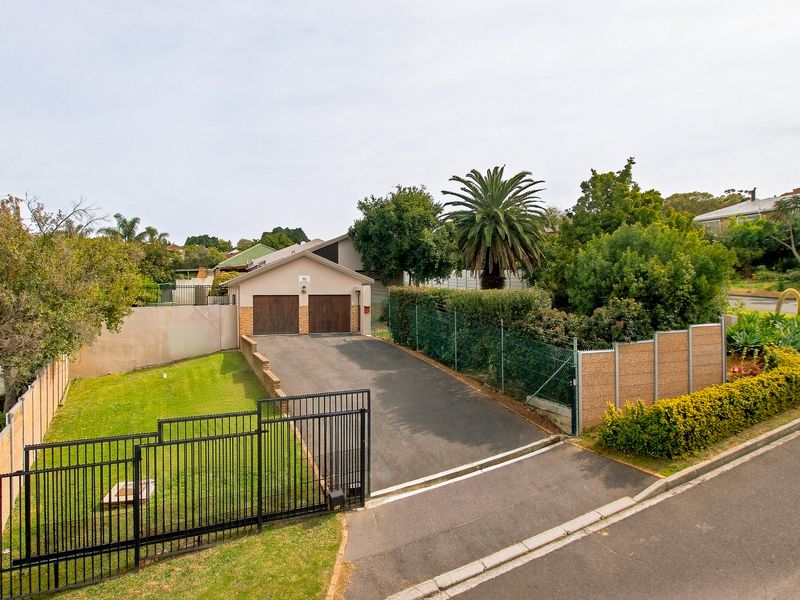 Elevated view of the property frontage featuring a double garage, paved driveway, and secure perimeter fencing with established garden landscaping.
