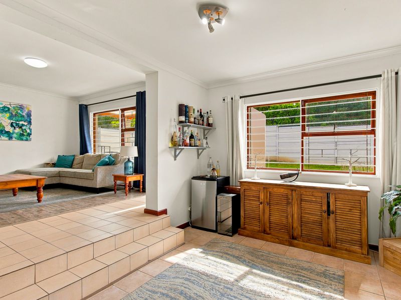 Open plan living area featuring tiled flooring, a stepped transition between levels, and large windows with security bars, offering a bright and functional layout.