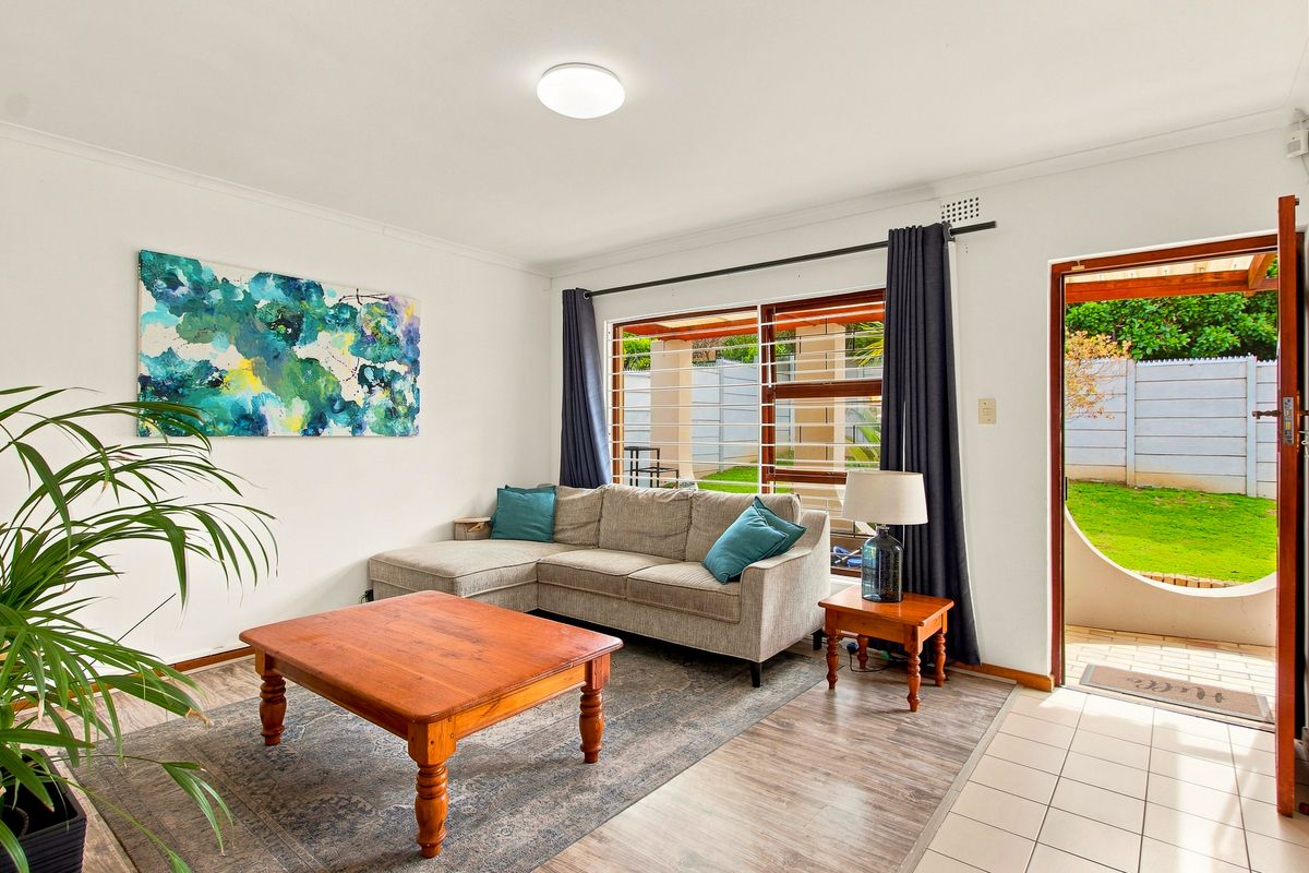A bright living room featuring a mix of tiled and laminate flooring, with direct access to an outdoor patio area through a sliding door.