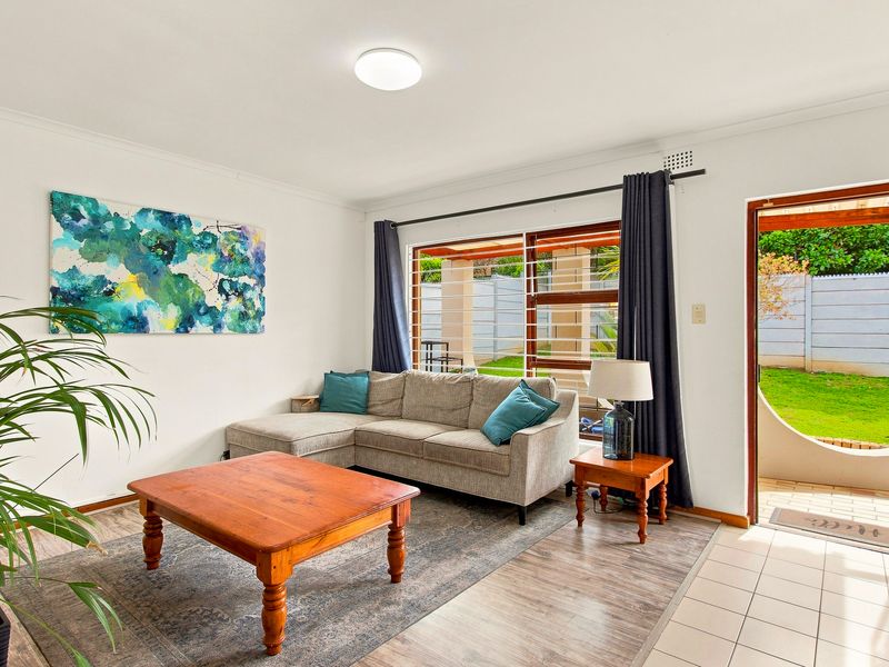 A bright living room featuring a mix of tiled and laminate flooring, with direct access to an outdoor patio area through a sliding door.