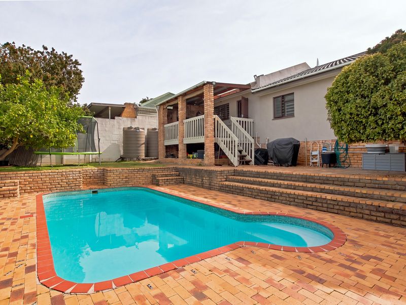 Outdoor entertainment area featuring a swimming pool, brick paved patio, raised retaining walls, and a covered patio with timber balustrades.