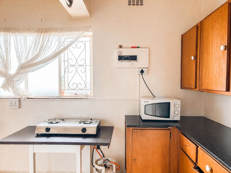 A dated kitchen featuring wooden cabinetry, dark laminate countertops, and a window with security bars. The space requires cosmetic updates to modernize the finishes.