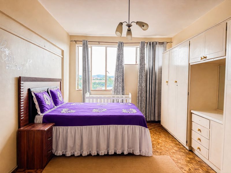 A bedroom featuring parquet flooring, a large built-in wardrobe with integrated drawers, and natural light from a window.