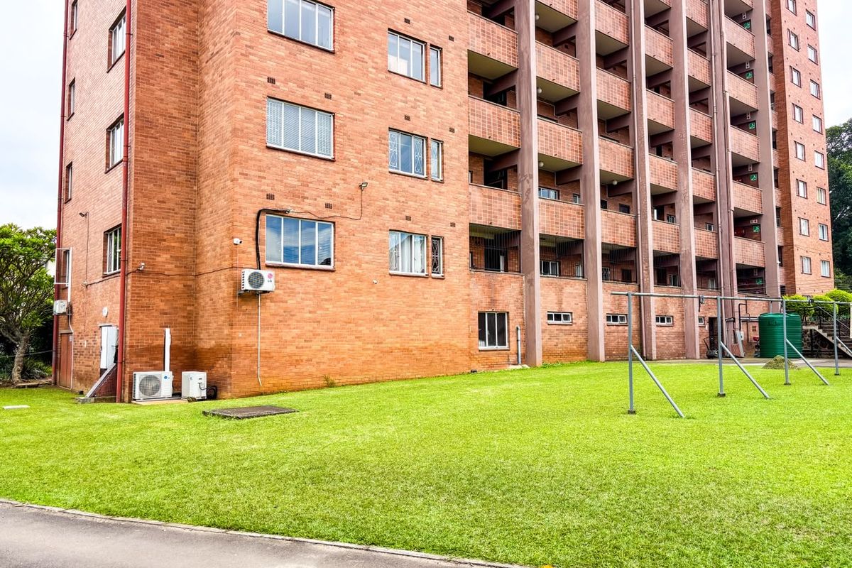 Rear view of a multi-story brick apartment building featuring private balconies, external air conditioning units, and a communal lawn area with washing lines.