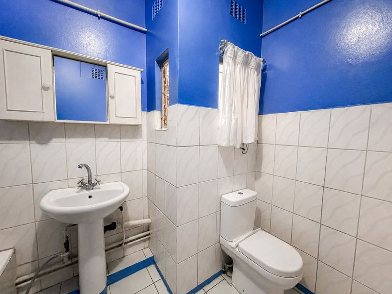A compact bathroom featuring a pedestal basin, toilet, and wall-mounted medicine cabinet with tiled finishes and exposed plumbing.
