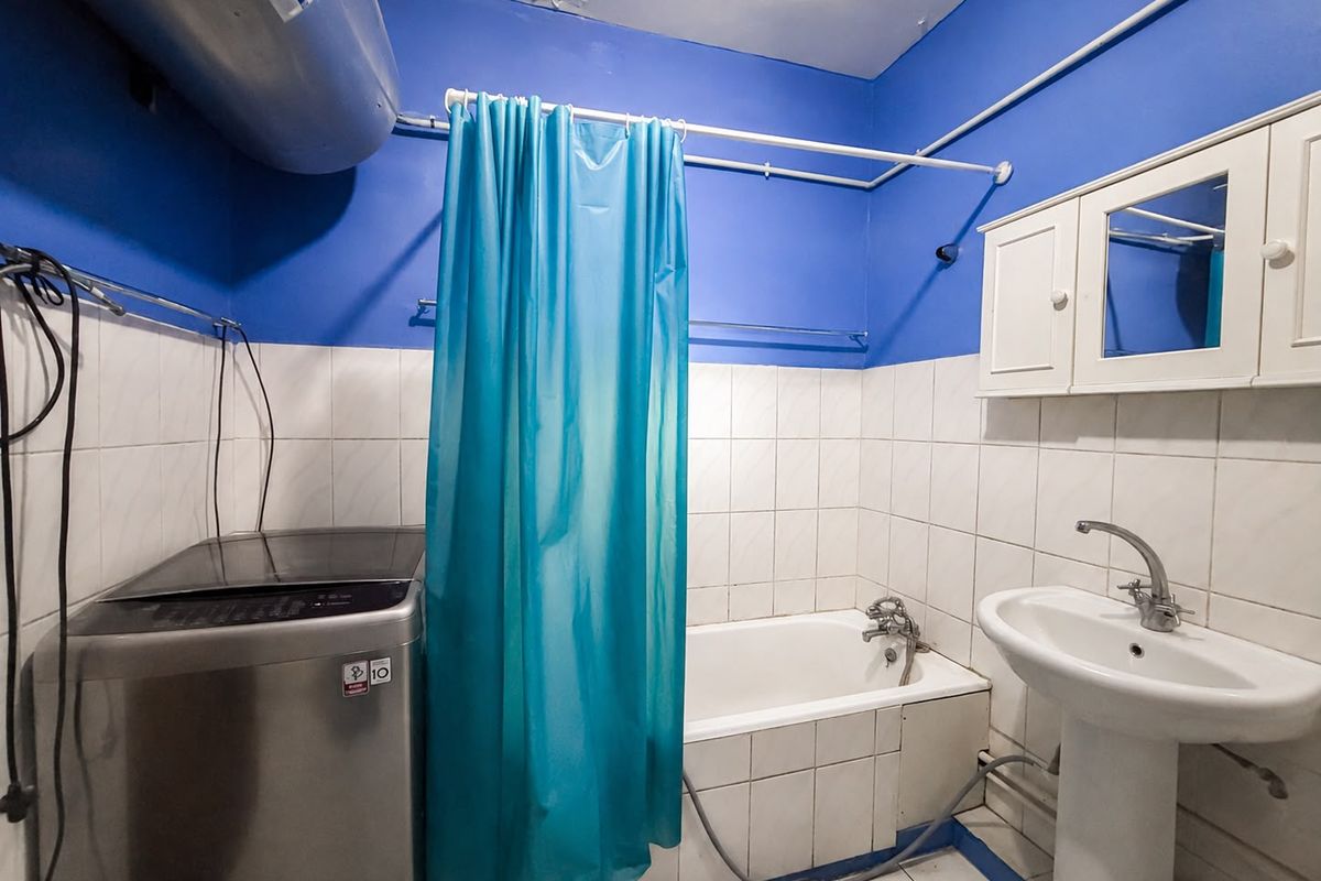Functional bathroom featuring a pedestal basin, bathtub with shower curtain, and wall-mounted storage cabinet, requiring cosmetic updates to the ceiling and wall finishes.