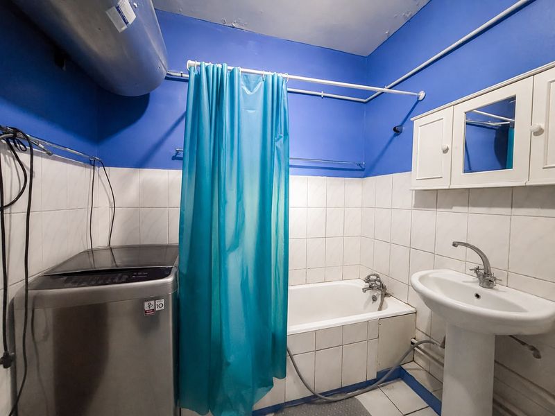 Functional bathroom featuring a pedestal basin, bathtub with shower curtain, and wall-mounted storage cabinet, requiring cosmetic updates to the ceiling and wall finishes.