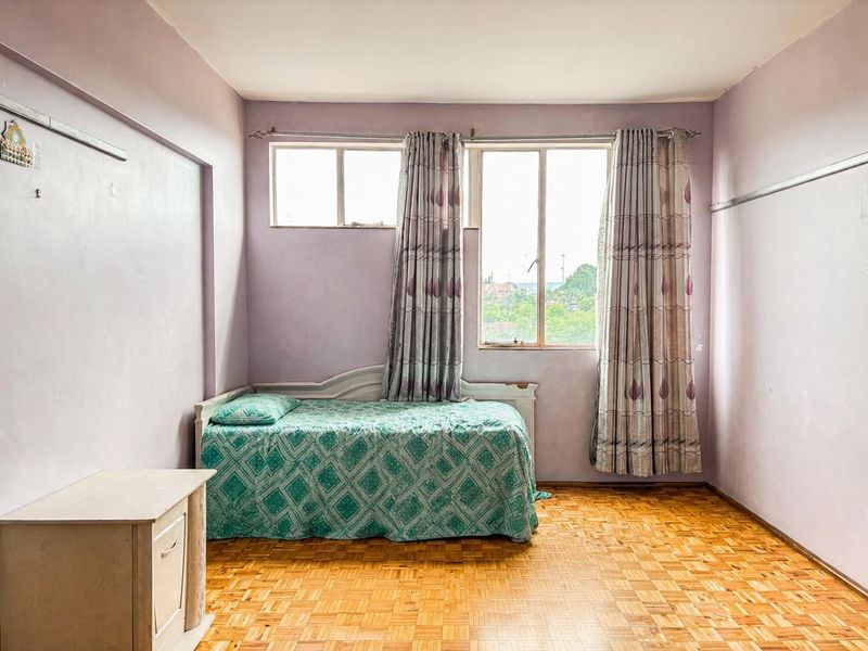 A bedroom featuring parquet flooring and aluminium-framed windows, offering a blank canvas for renovation with potential for modern updates.