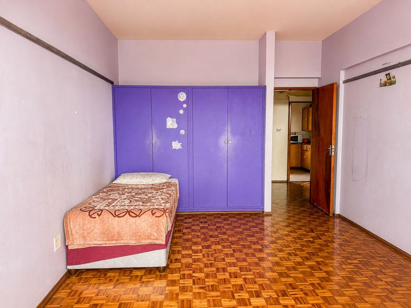 A bedroom featuring parquet flooring, built-in purple cupboards, and a picture rail, with a view into the adjacent kitchen area.