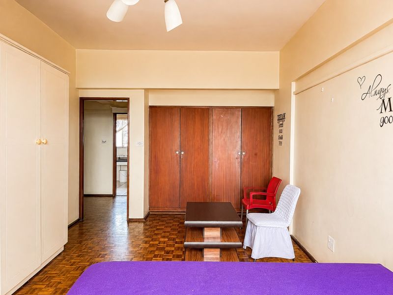 Bedroom featuring parquet flooring and extensive built-in wooden wardrobe storage, with an adjoining doorway leading to a secondary space.
