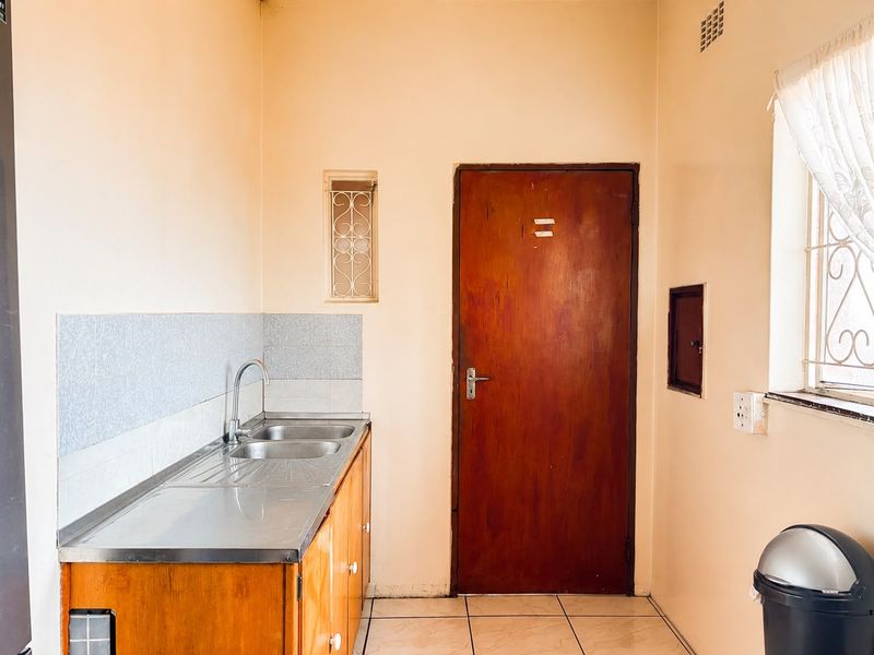 A compact kitchen area featuring a stainless steel sink, wooden cabinetry, tiled splashback, and tiled flooring, offering a functional space ready for modernization.
